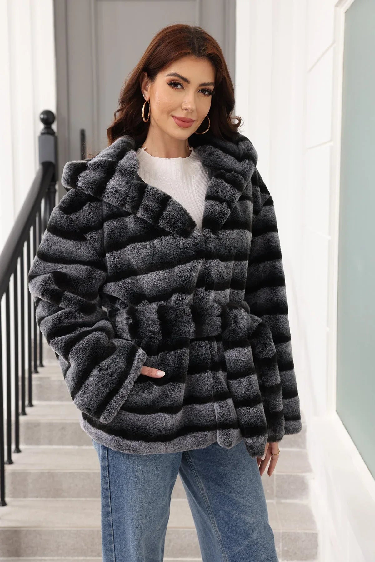 Front view of a woman in a hooded, belted, grey and black striped faux fur jacket.
