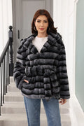 Woman wearing a hooded, belted, grey and black striped faux fur jacket with jeans.