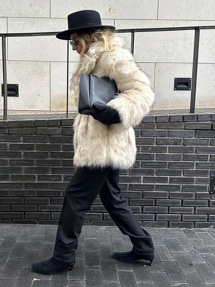 Side view of a woman wearing a cream-colored faux fur coat and black pants.