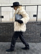 Side view of a woman wearing a cream-colored faux fur coat and black pants.