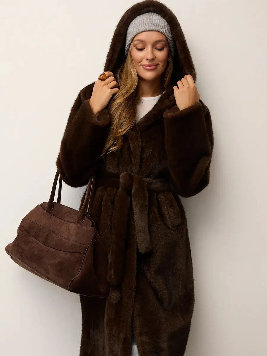 Woman wearing a brown faux fur hooded coat and holding a brown handbag.