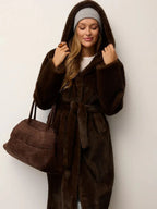 Woman wearing a brown faux fur hooded coat and holding a brown handbag.