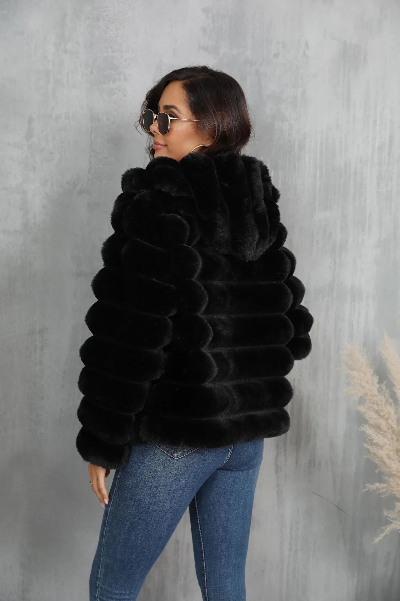 Back view of a woman in a black hooded faux fur jacket with horizontal stripe pattern.