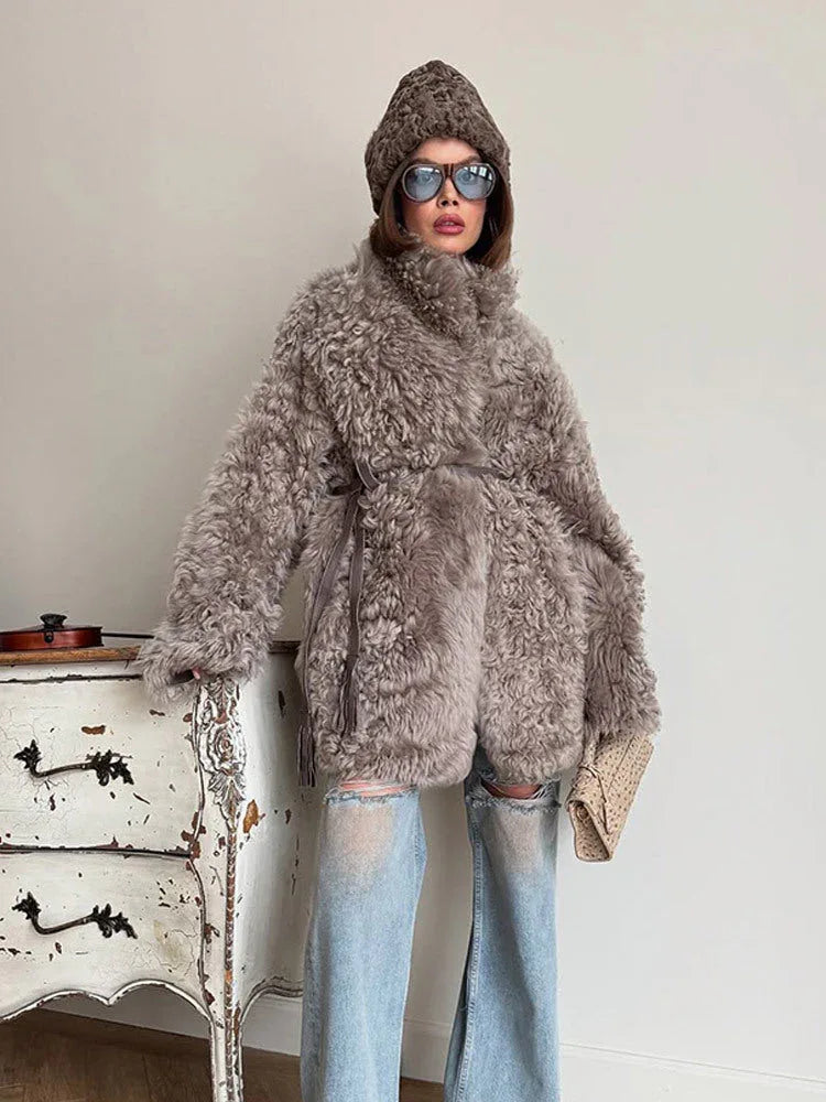 Full body shot of a woman styled in a grey curly faux fur coat, paired with casual denim and accessories.