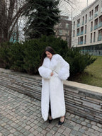 Woman in a white faux fur coat adjusting the front of the garment.