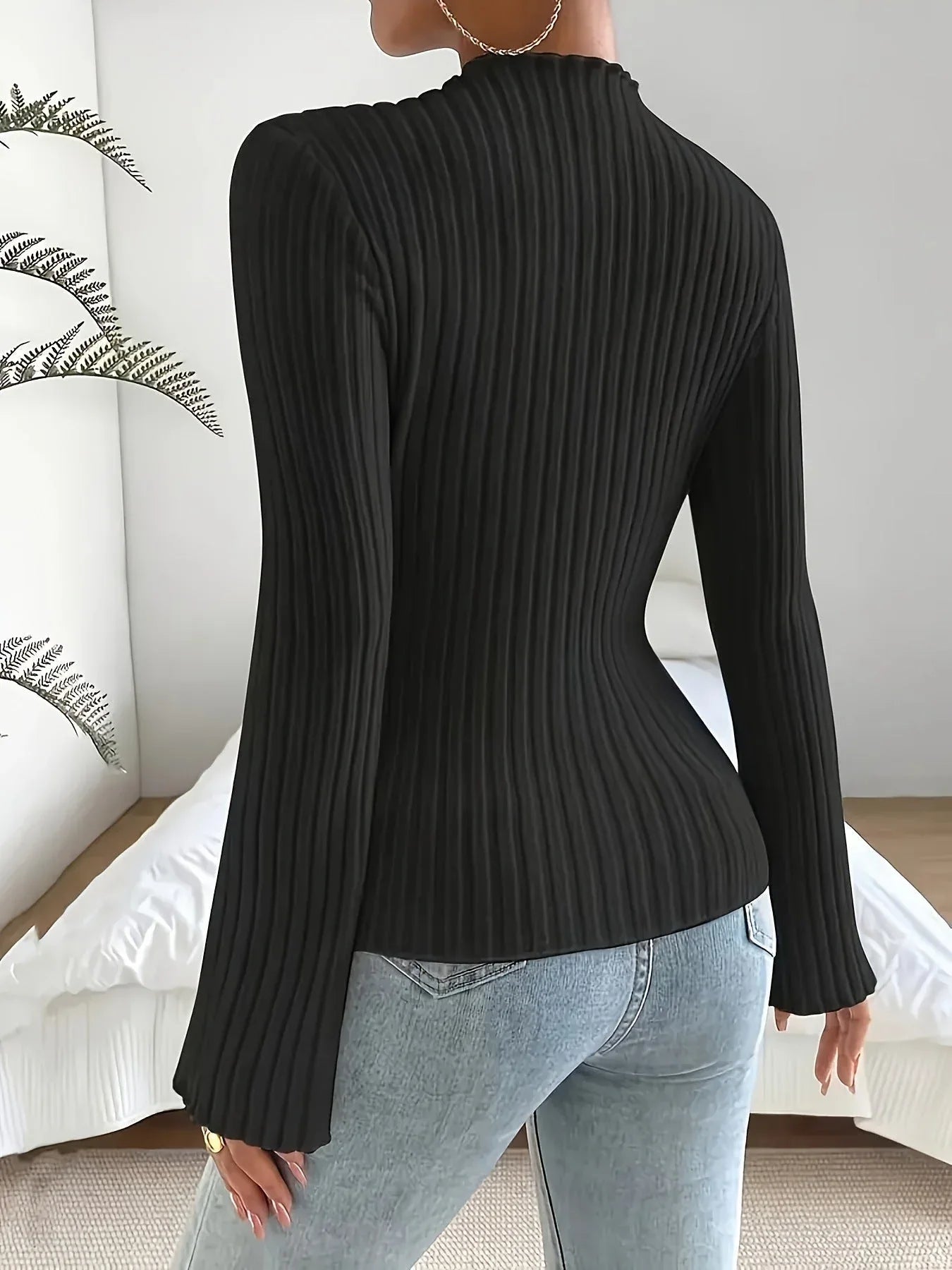 Back view of a woman in a black ribbed knit long-sleeve top with flared sleeves and a mock neckline, paired with blue jeans.