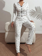 Woman sitting on a bed, showing the full pink heart print pajama set.
