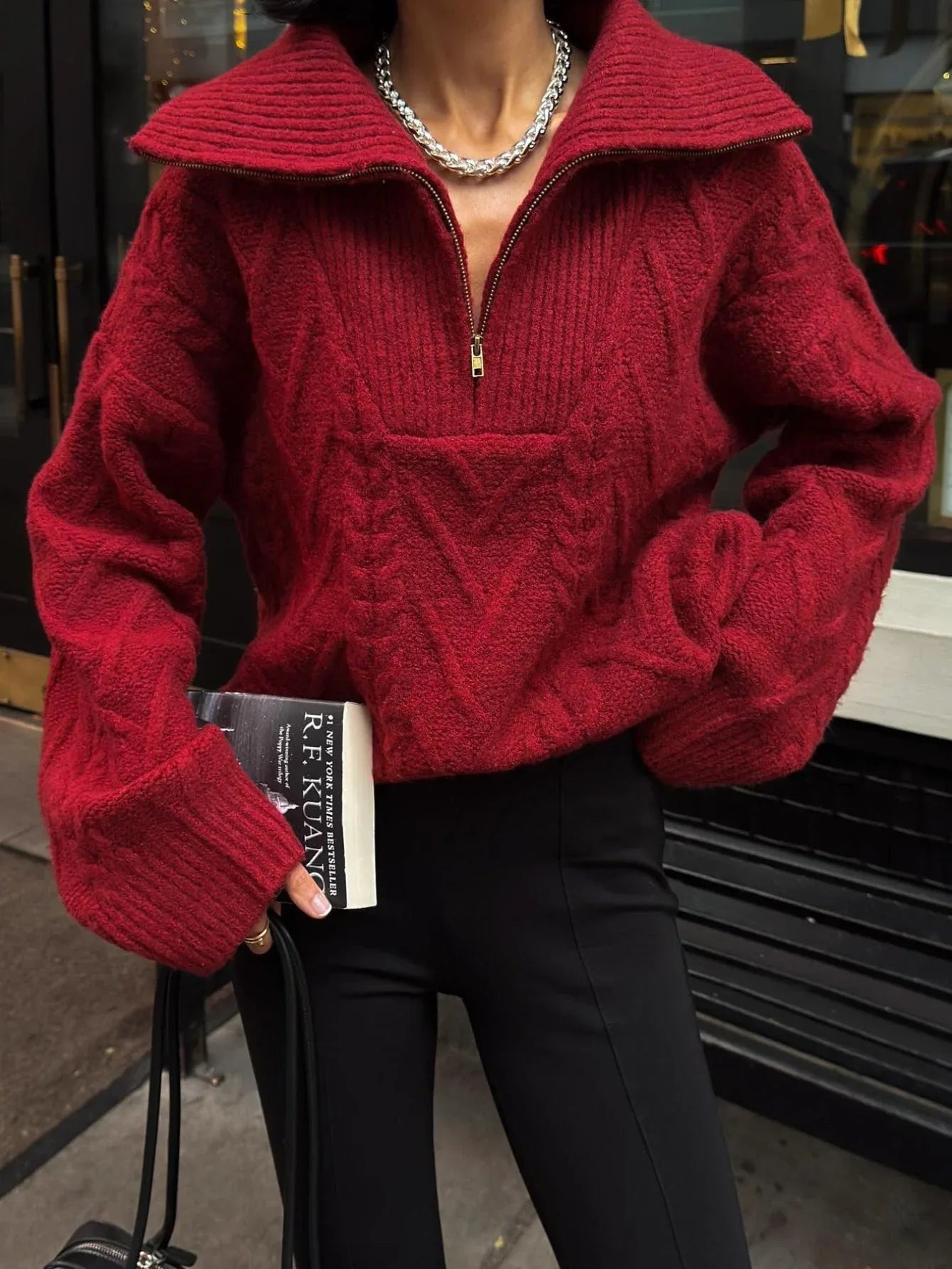 Close-up of a woman wearing a red textured knit half-zip sweater with cable knit patterns and a spread collar.