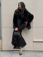 Woman posing in a black faux fur jacket and black dress.