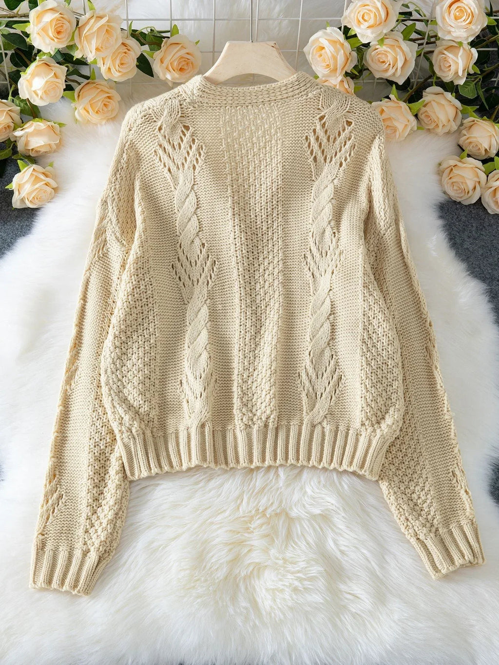 Back view of a beige cropped knit cardigan laid flat, showcasing the knit pattern.