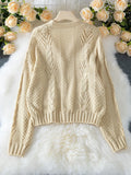 Back view of a beige cropped knit cardigan laid flat, showcasing the knit pattern.