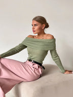 Woman wearing a green off-the-shoulder ribbed knit sweater with long sleeves.