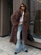 Full body shot of a woman in a long brown shaggy faux fur coat, white t-shirt, and wide-leg jeans, standing outdoors.