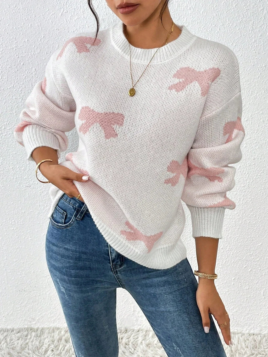 Woman in a white knit sweater with a pink bow print, showing off the relaxed fit.