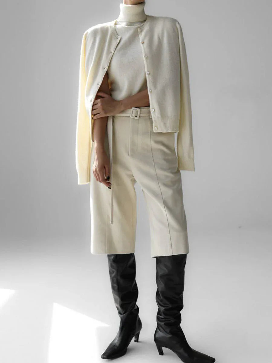 Woman wearing a cream-colored fine knit cardigan over a cream turtleneck and cream culottes with black boots