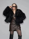 Full body shot of a woman posing in a black shaggy faux fur jacket, brown faux leather wrap dress, sheer black tights, and black knee-high boots