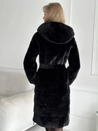 Back view of a woman in a black faux fur coat with a hood and belted waist.