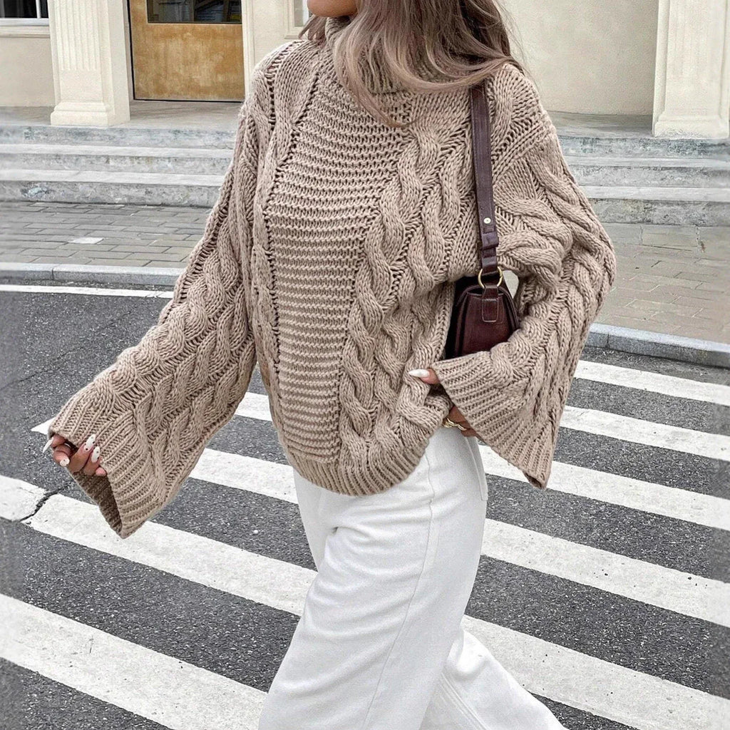 Close-up of a woman wearing a beige cable knit sweater and white jeans.