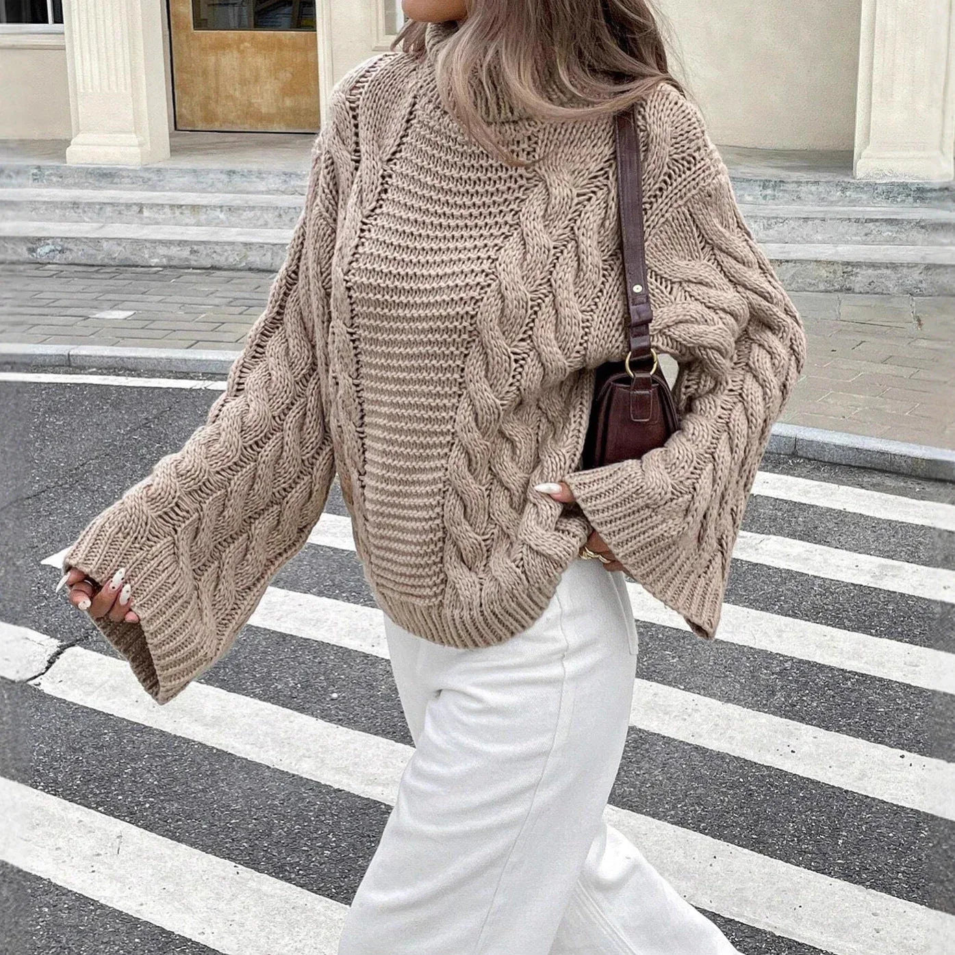 Close-up of a woman wearing a beige cable knit sweater and white jeans.