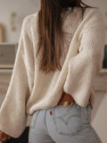 Back view of a woman in a cream knit cardigan with long, voluminous sleeves.