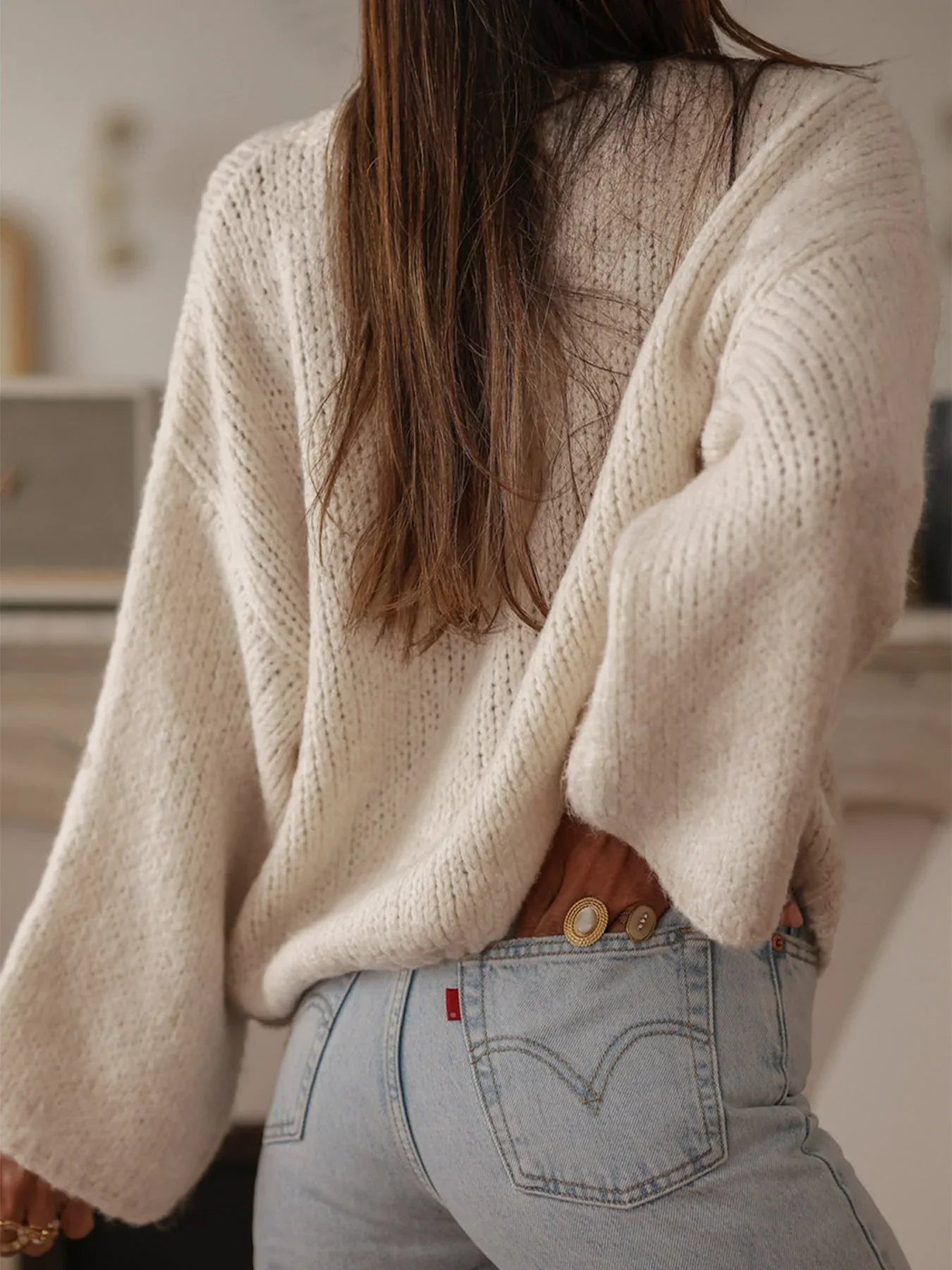 Back view of a woman in a cream knit cardigan with long, voluminous sleeves.