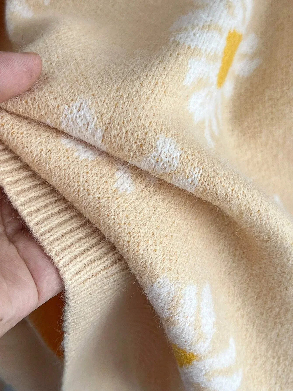 Close-up of the knitted fabric of a light yellow cardigan with a white daisy print.