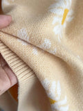 Close-up of the knitted fabric of a light yellow cardigan with a white daisy print.