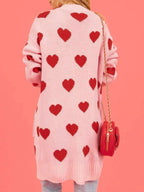 Back view of a woman wearing a pink knit cardigan with a repeating red heart motif.