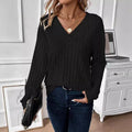 Woman holding a black handbag while wearing a black ribbed sweater.