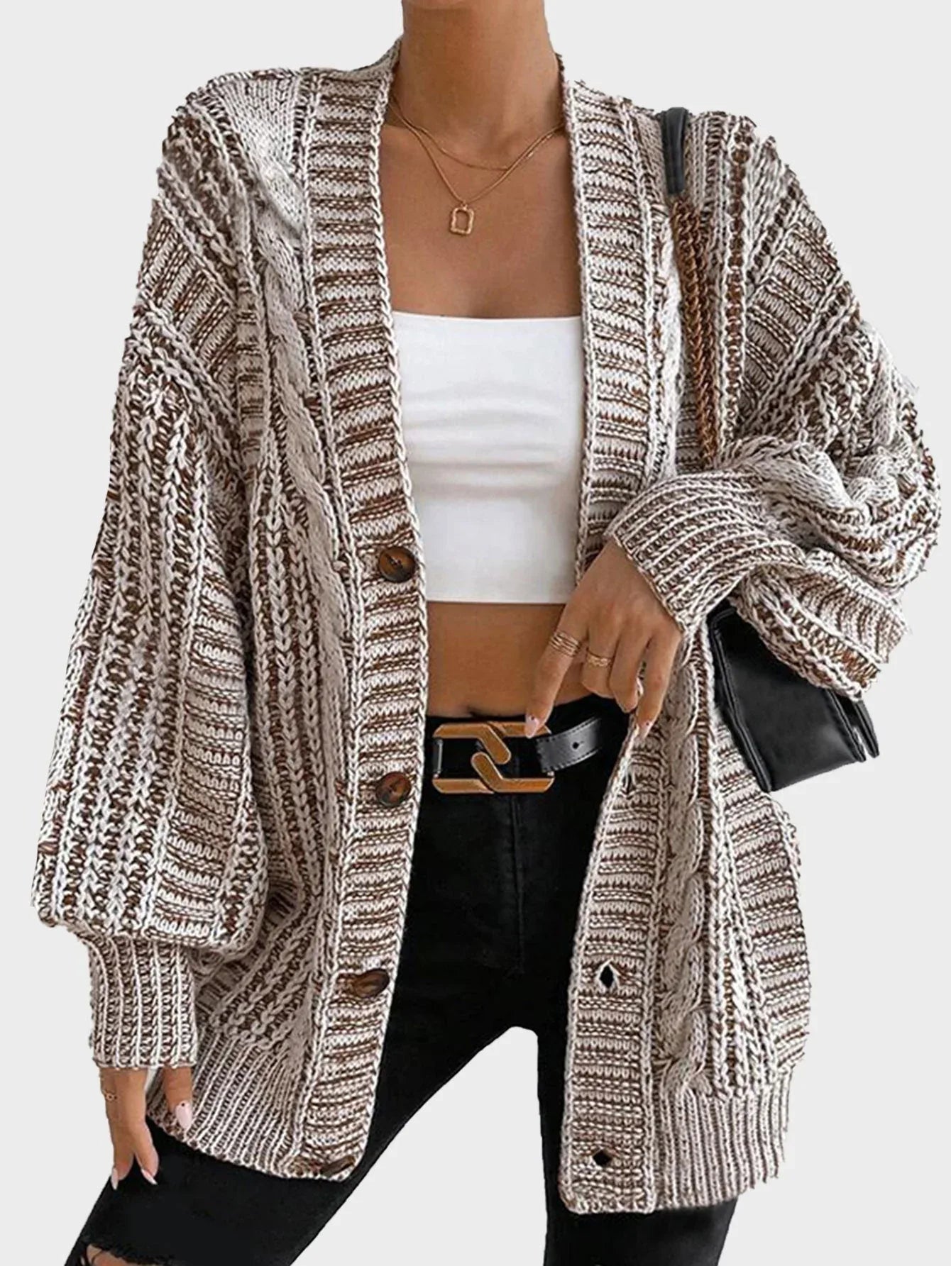 Woman wearing a cream oversized chunky knit cardigan with two front pockets and long balloon sleeves.