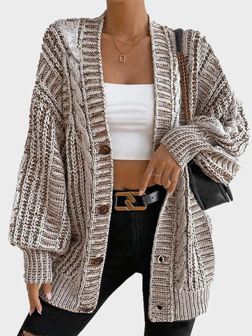 Woman wearing a cream oversized chunky knit cardigan with two front pockets and long balloon sleeves.