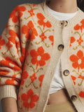 Detail shot of the buttons and neckline of a beige cardigan with an orange floral print.