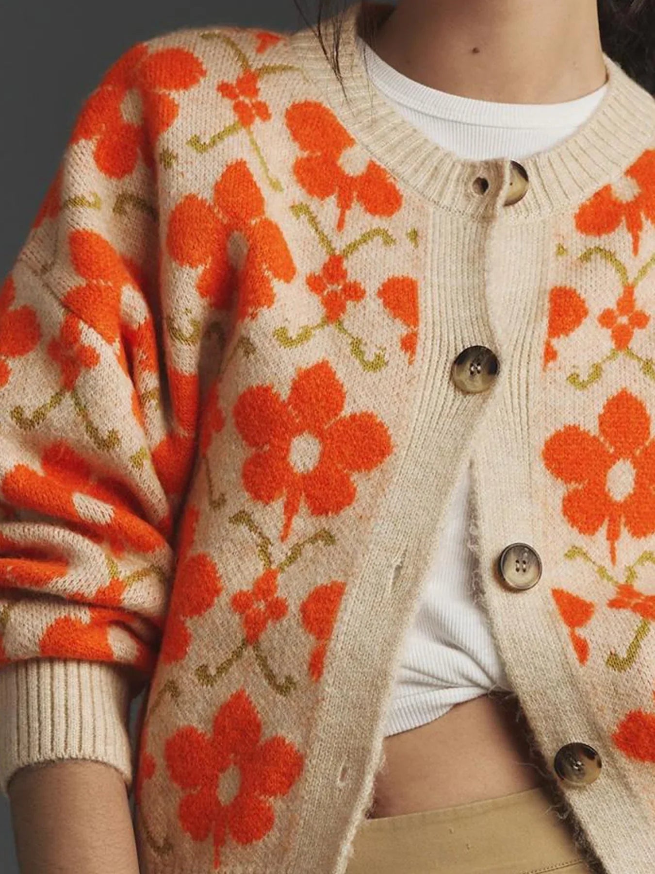 Detail shot of the buttons and neckline of a beige cardigan with an orange floral print.