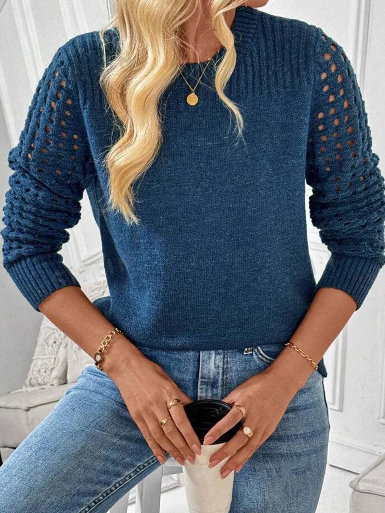 Close-up of a woman wearing a blue knit sweater with openwork sleeves and holding a coffee cup