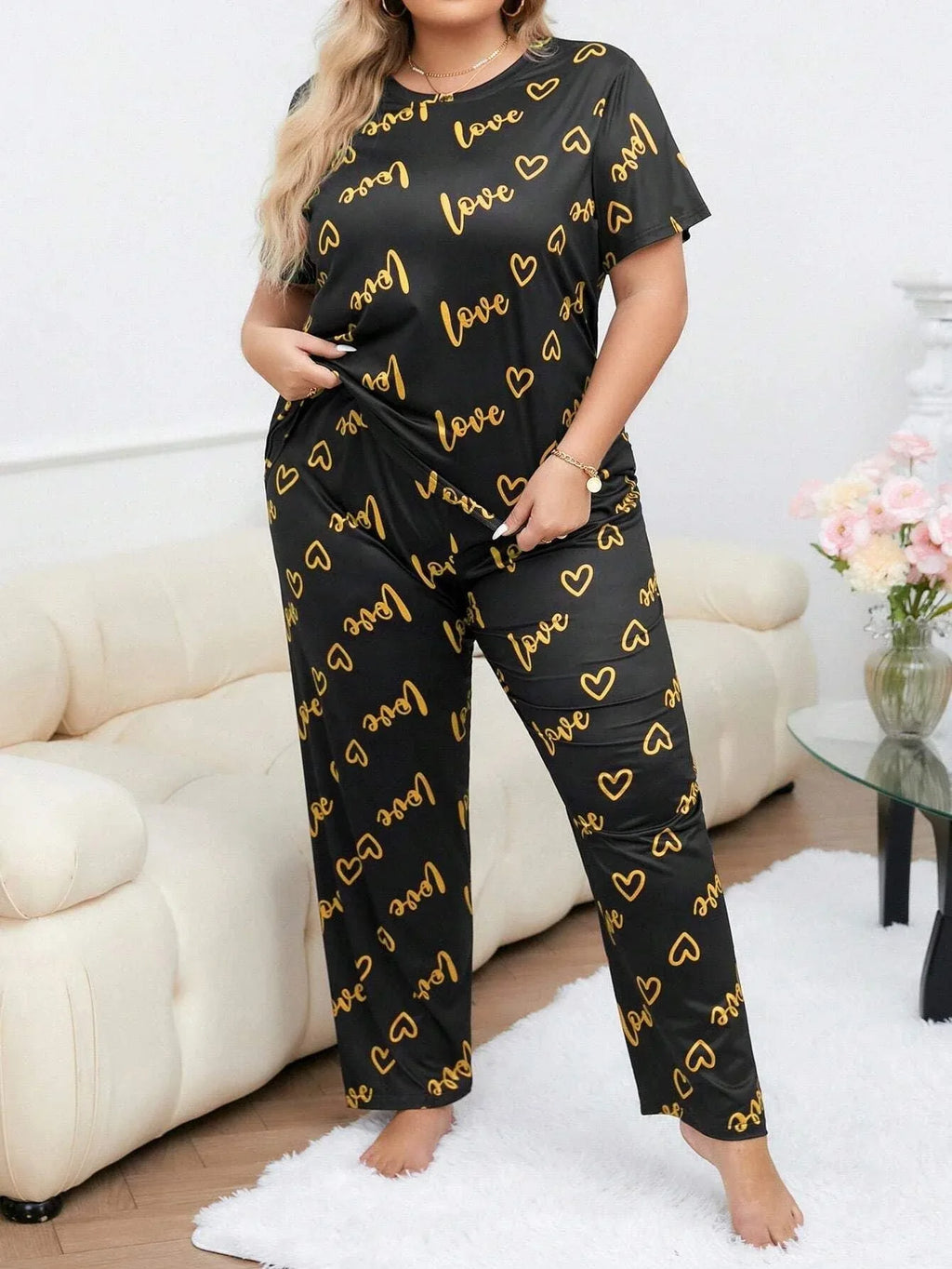 Woman wearing a black short-sleeve pajama top and pants with a gold heart and 'love' graphic print, standing.