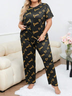 Woman wearing a black short-sleeve pajama top and pants with a gold heart and 'love' graphic print, standing.