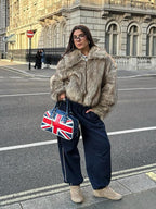 Woman wearing a brown faux fur jacket with a collared neckline and zipper closure, paired with navy track pants and sneakers.