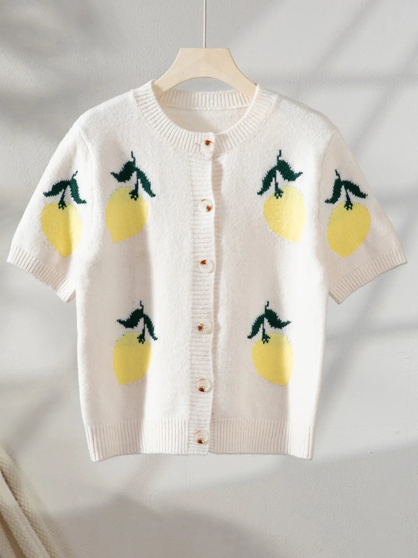 Cream knit cardigan with a lemon print hanging on a hanger