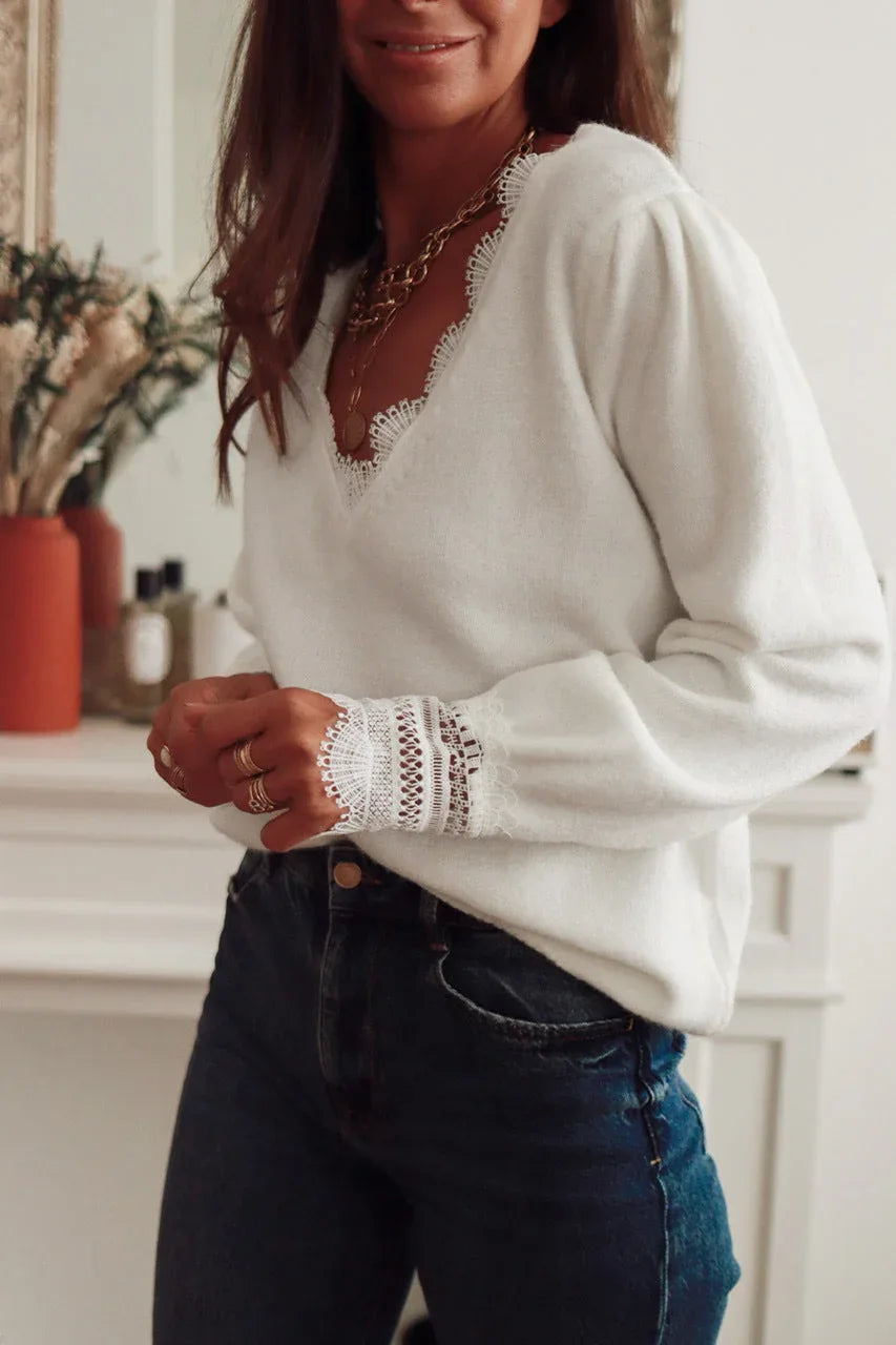 Side view of a woman in a white knit sweater with lace accents, styled with gold necklaces and blue jeans.