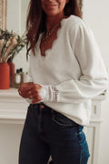 Side view of a woman in a white knit sweater with lace accents, styled with gold necklaces and blue jeans.