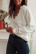 Side view of a woman in a white knit sweater with lace accents, styled with gold necklaces and blue jeans.