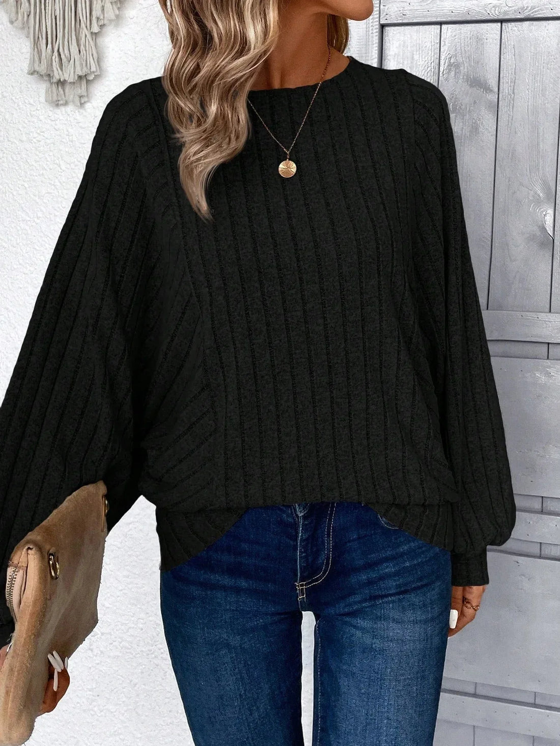 Woman wearing a black ribbed knit sweater with wide sleeves and round neckline, paired with blue jeans.