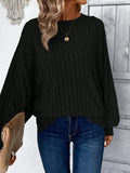 Woman wearing a black ribbed knit sweater with wide sleeves and round neckline, paired with blue jeans.