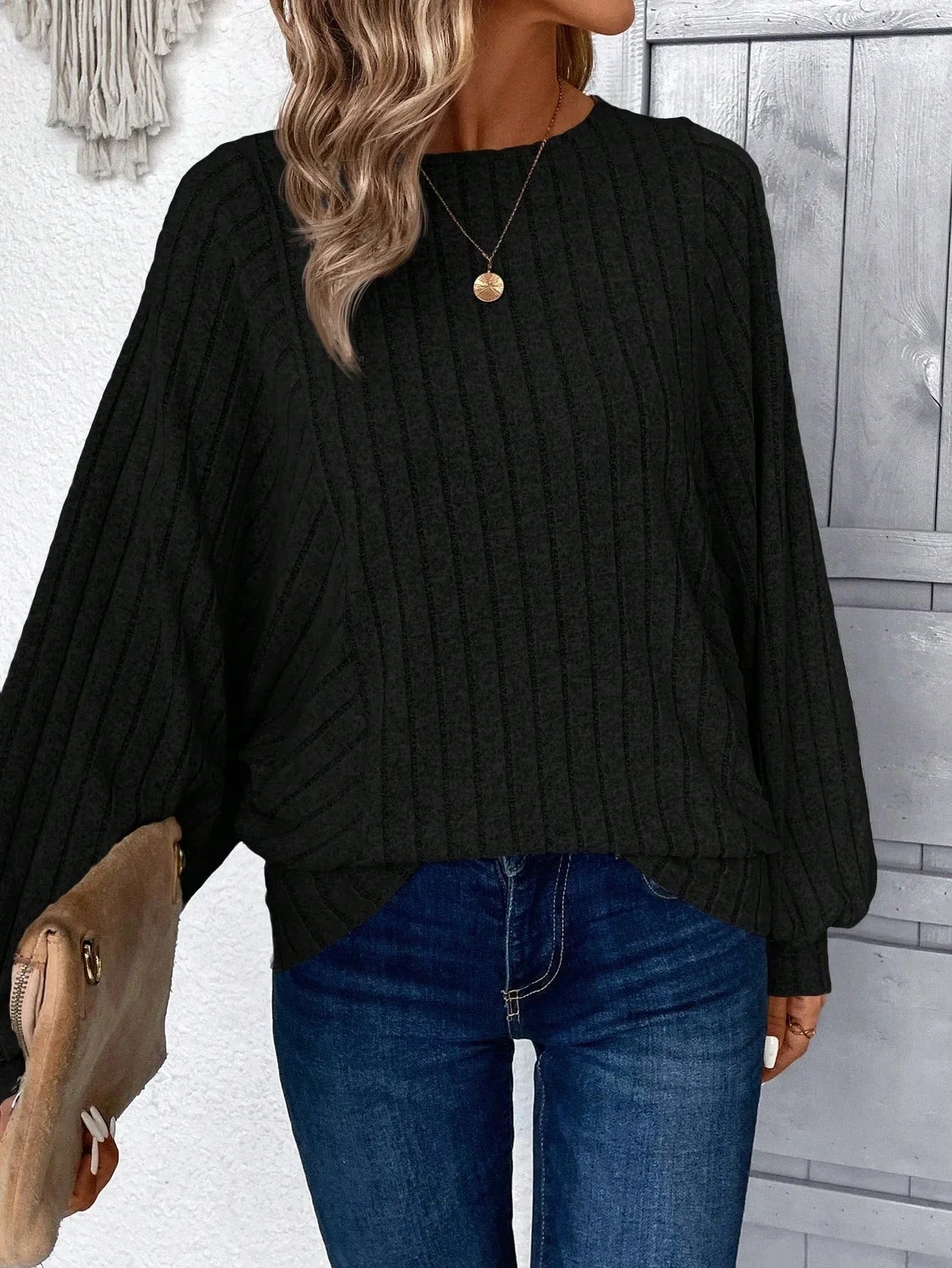 Woman wearing a black ribbed knit sweater with wide sleeves and round neckline, paired with blue jeans.