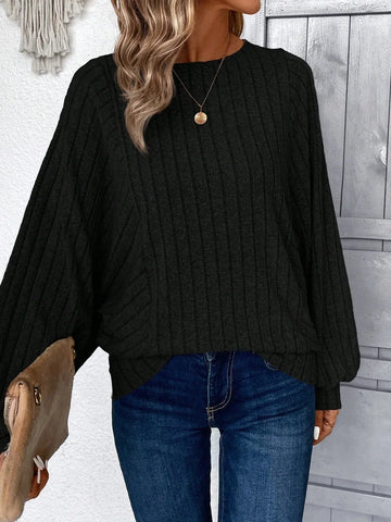 Woman wearing a black ribbed knit sweater with wide sleeves and round neckline, paired with blue jeans.