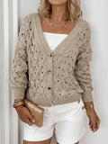Model styling a beige open-knit cardigan with white shorts and gold accessories.
