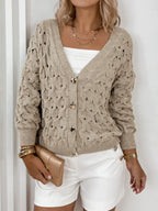 Model styling a beige open-knit cardigan with white shorts and gold accessories.