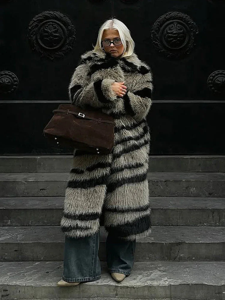 Woman standing on steps holding a handbag, wearing a striped faux fur coat and jeans.