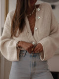Close-up of a woman's hands adjusting the buttons on a cream knit cardigan.