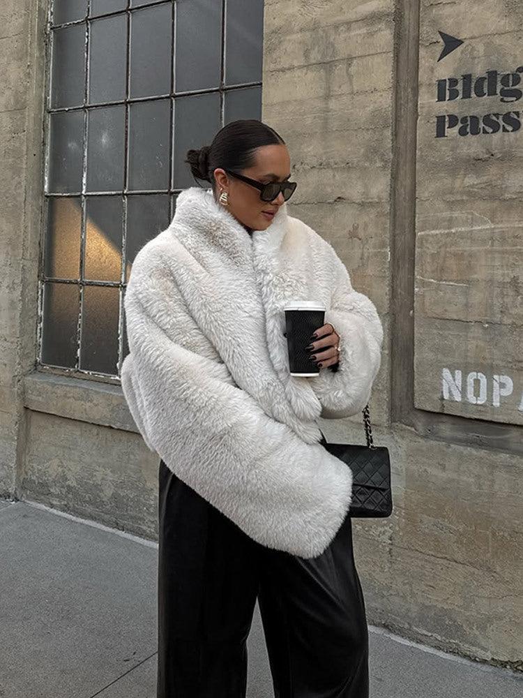 Woman in a white faux fur jacket holding a coffee cup and a black quilted handbag.